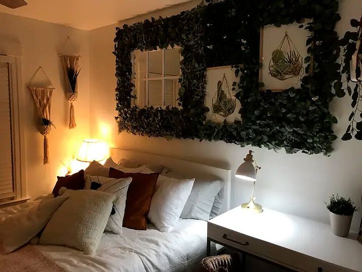 The larger bedroom is decorated in a boho chic style with verdant plant life and light, airy colors. It also has a dedicated workspace.
