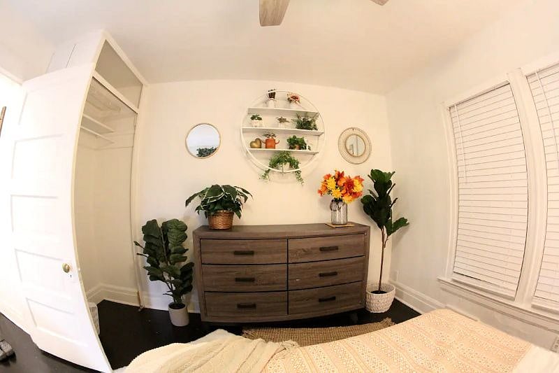 The larger bedroom is decorated in a boho chic style with verdant plant life and light, airy colors. It also has a dedicated workspace.