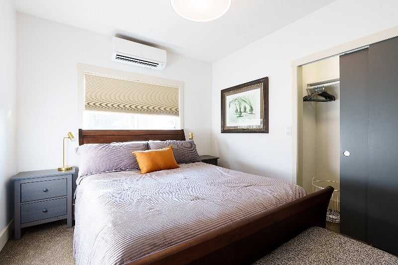 South bedroom with blackout shades, reading lamps, bench at foot of the bed, and heat pump for heat or air conditioning.