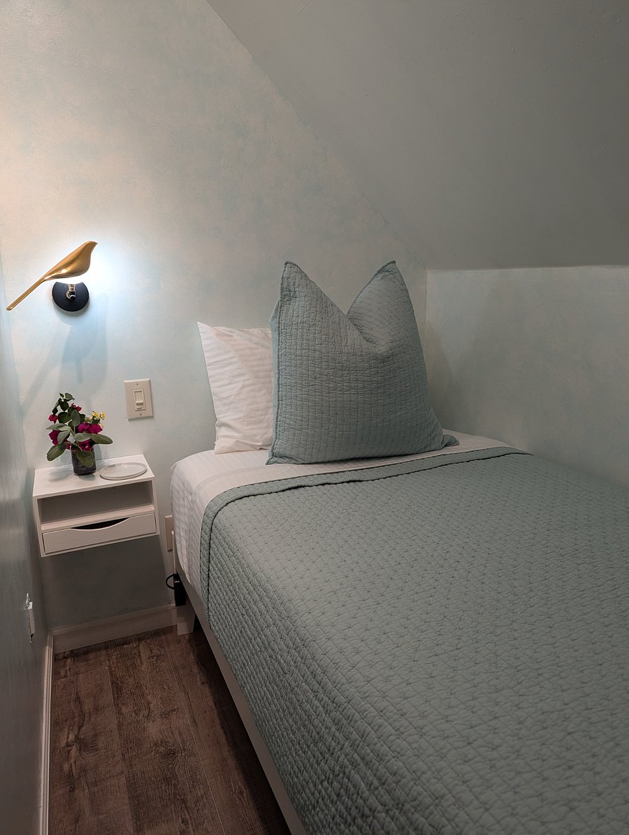 Sleeping nook with essentials - bed, light, hooks for clothing and backpack, small bench to sit on.