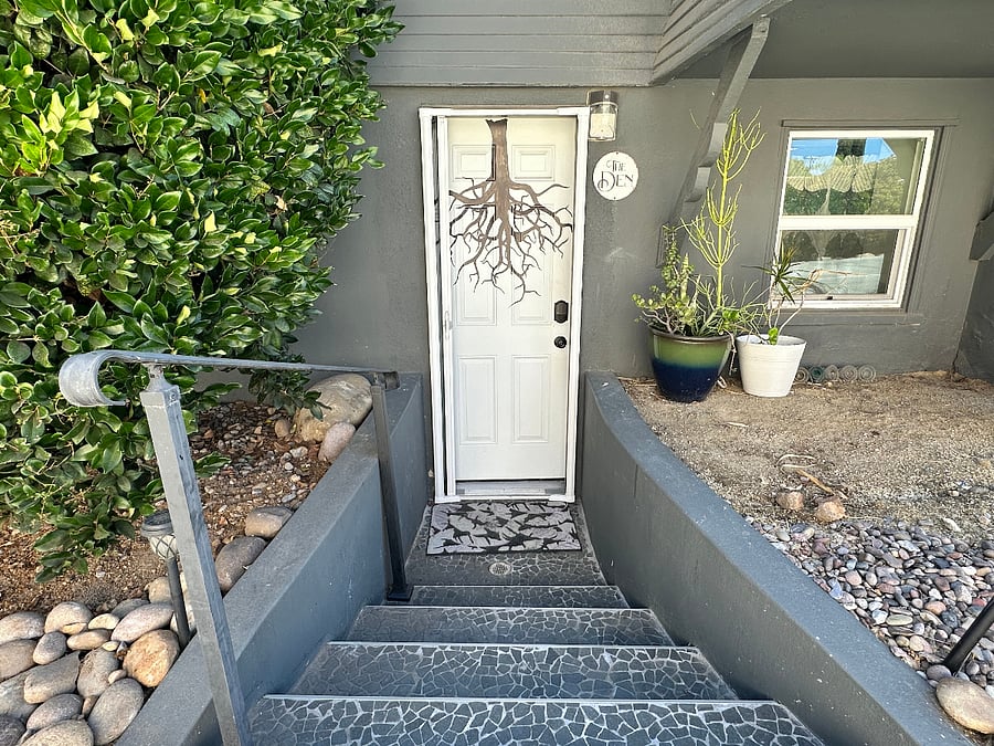 The entrance to the Den is on the side of the main house, garden level, facing the driveway (white door with tree root design and "Den" sign next to it)
