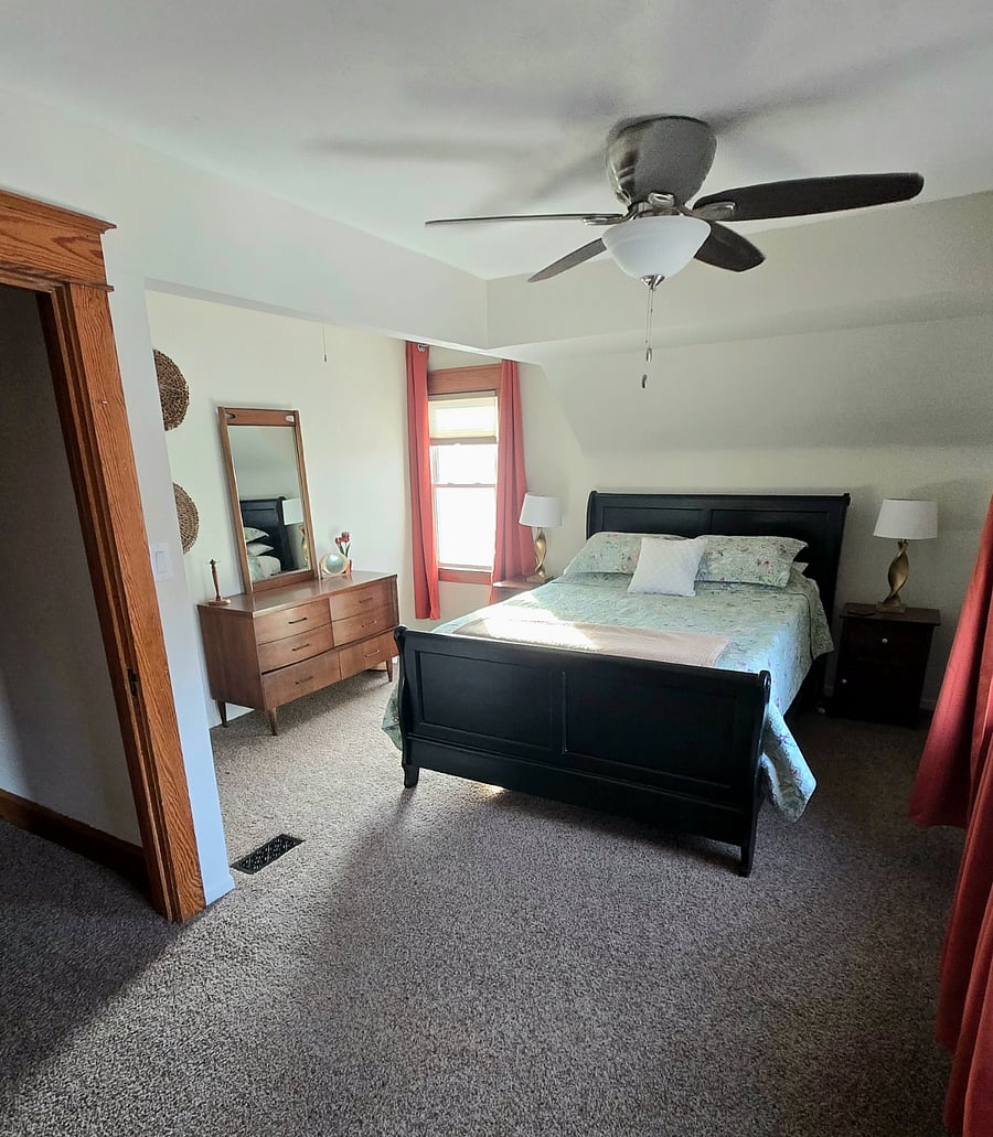 Bedroom with queen bed, blackout curtains, dresser and walk in closet.