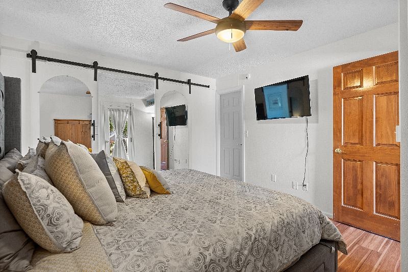 Bedroom with king size bed. Dresser drawers are discretely stored underneath the bed. New flat screen TV on the wall. White door leads to laundry and closet.