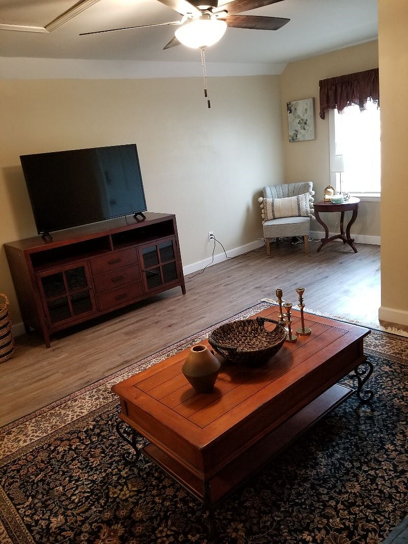 Living room, tv stand, couch with 2 side tables and sitting area, ceiling fan.