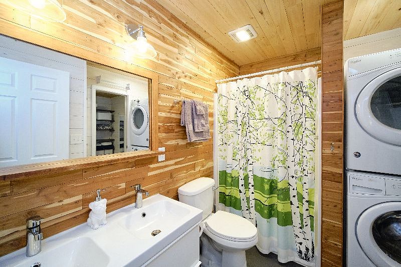 Bathroom with two-sink vanity, toilet, walk-in shower, and washer and dryer.