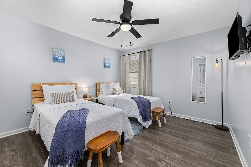 Relaxing guest bedroom with two comfortable twin-size beds, alarm clock, 32-in smart tv, closet with storage, and ceiling fan