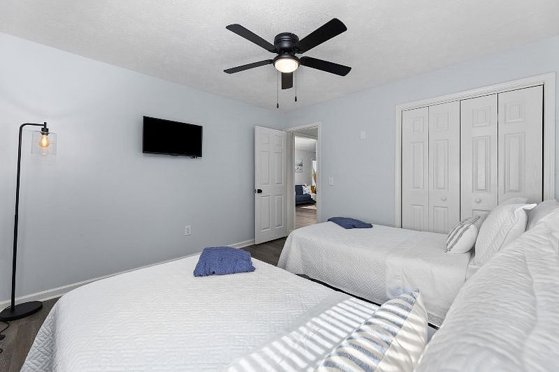 Relaxing guest bedroom with two comfortable twin-size beds, alarm clock, 32-in smart tv, closet with storage, and ceiling fan