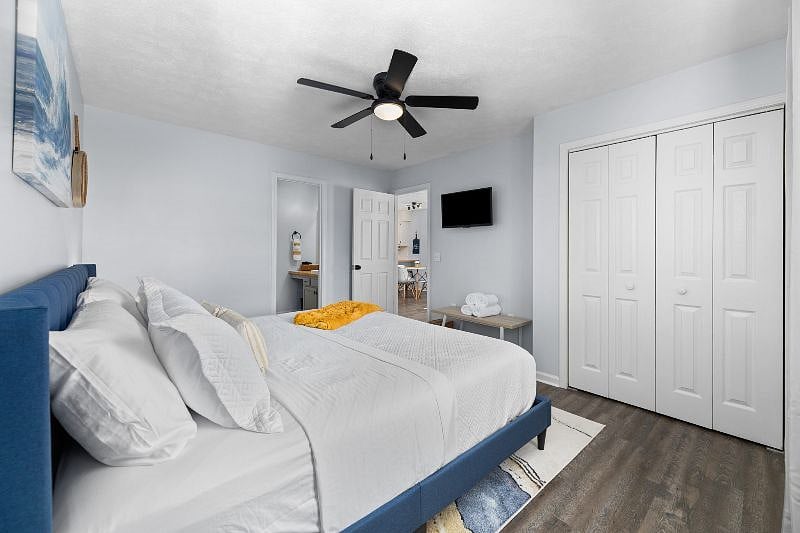 Warm and inviting main bedroom with a comfortable king-size bed, alarm clock, 32-in smart tv, closet with storage, and ceiling fan