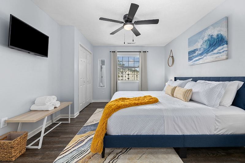 Warm and inviting main bedroom with a comfortable king-size bed, alarm clock, 32-in smart tv, closet with storage, and ceiling fan