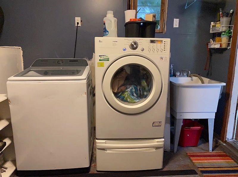 Washer, dryer, and wash bin with laundry essentials in garage.