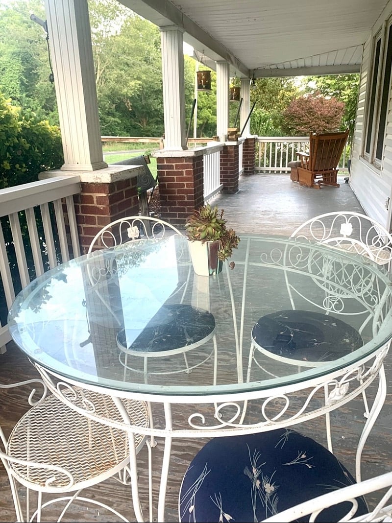 Covered porch with dining table, rocking chair, and gas grill.