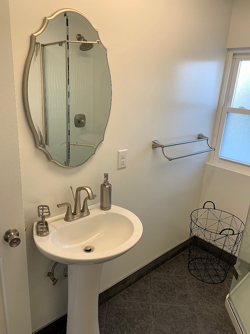 Bathroom sink, soap dispenser, toothbrush holder, mirror, towel holder, hamper.