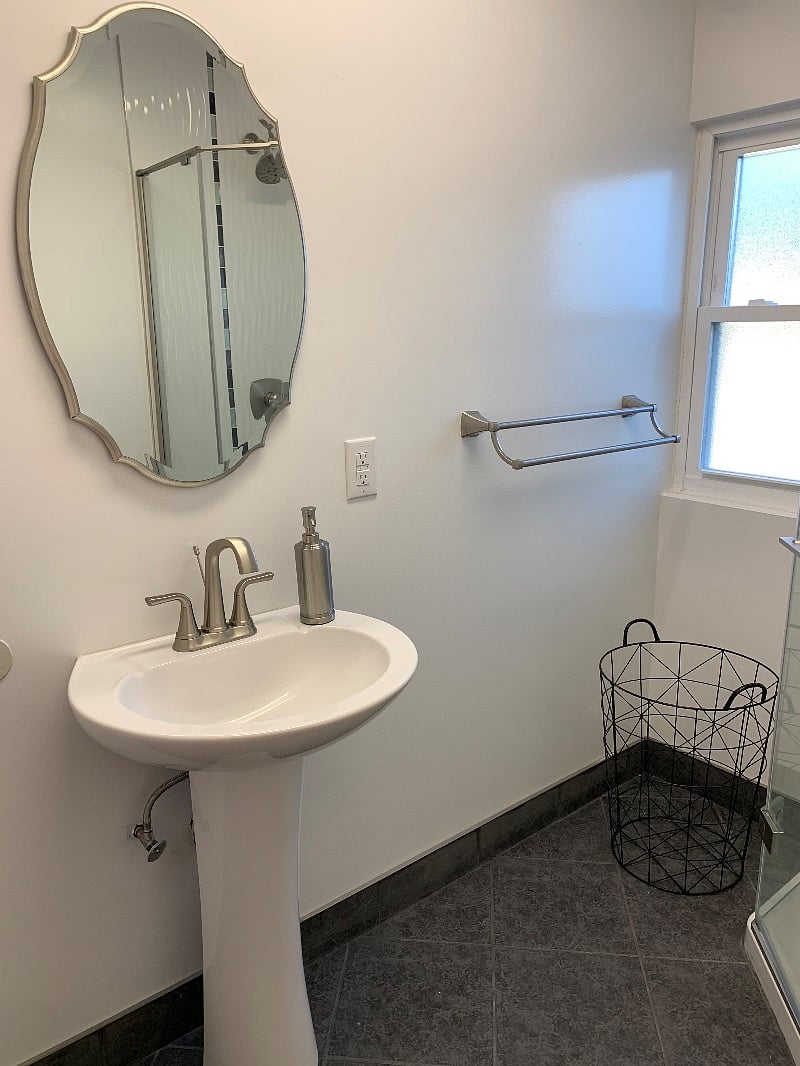 Bathroom sink, soap dispenser, mirror, towel holder, hamper.