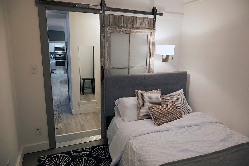 Double Sealy Posture-Pedic bed with upholstered headboard, provided linens and wall lamp.