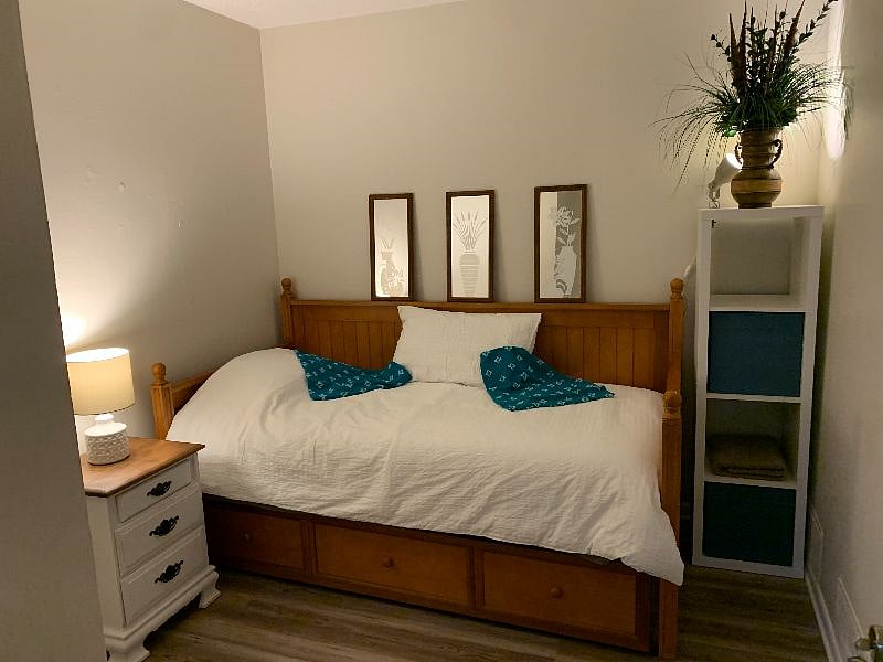 Cozy bedroom with a single bed, nightstand, lamp, shelving unit & closet to hang your clothes