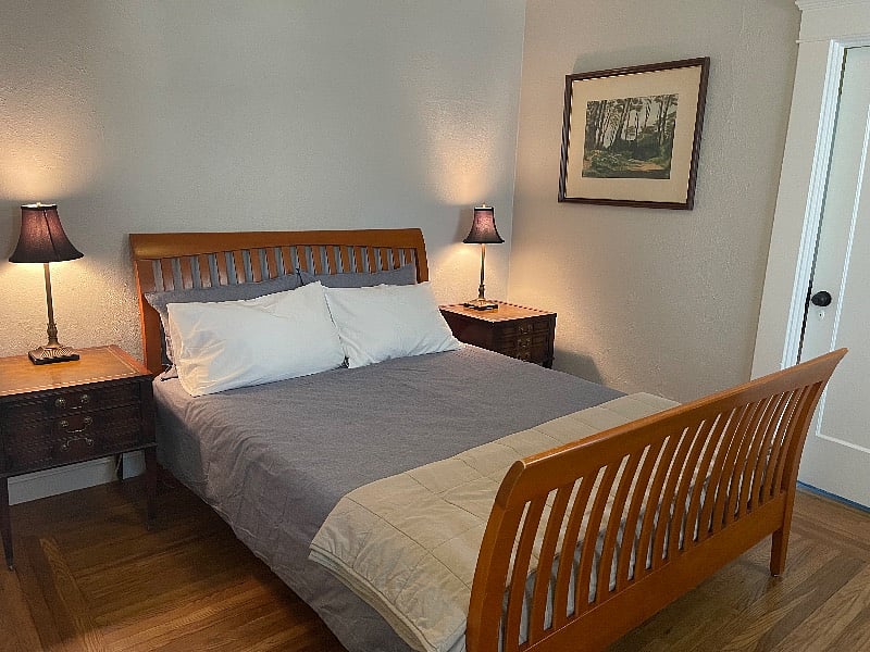 Main bedroom with queen bed, nightstands, and lamps. Door opens into back hallway.