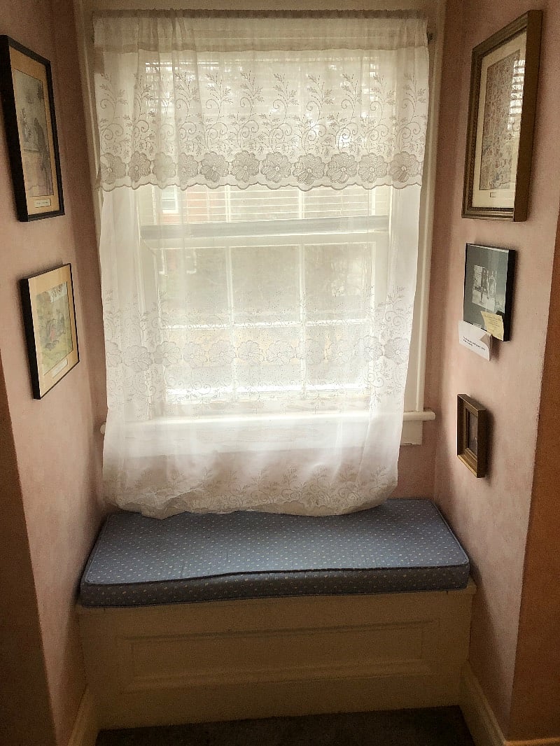 Window seat with cushion cover. Window has blinds and curtain.