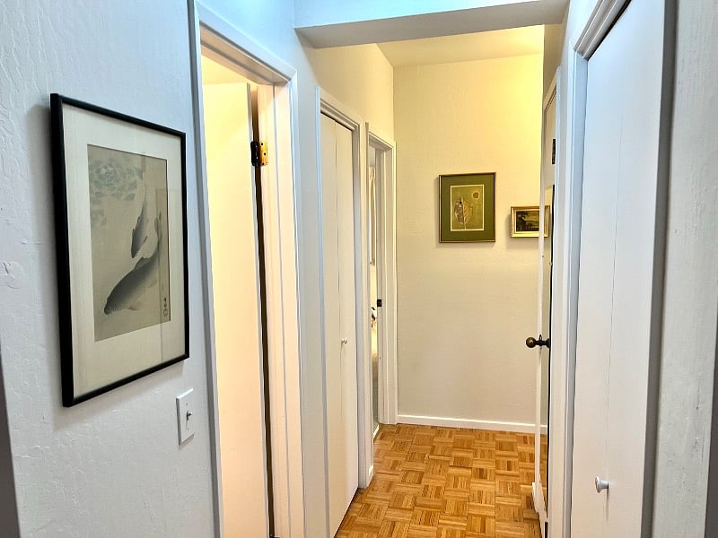 Hallway with half bathroom on left, laundry machine on left, coat closet on right. Bedrooms at end of hallway