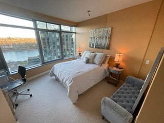 Bedroom with Queen bed and large double closet and a wall of windows looking to the river. Cut out on left shows where TV hangs on wall and a chair or in this casse a work desk can be placed