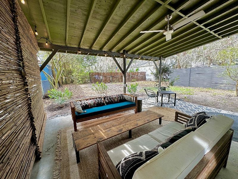 Outdoor covered patio with outdoor fan, bamboo partition wall, cafe lighting, 2 teak sofas and small bistro table.