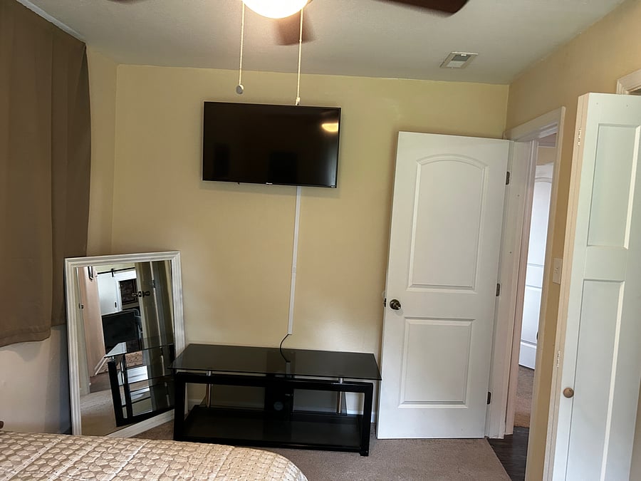 This is Bedroom 3 that has a Queen size bed a window with a street view and a 40 " Smart TV with a swivel head mounted on the wall. Located at the end of the hallway straight down to the door.