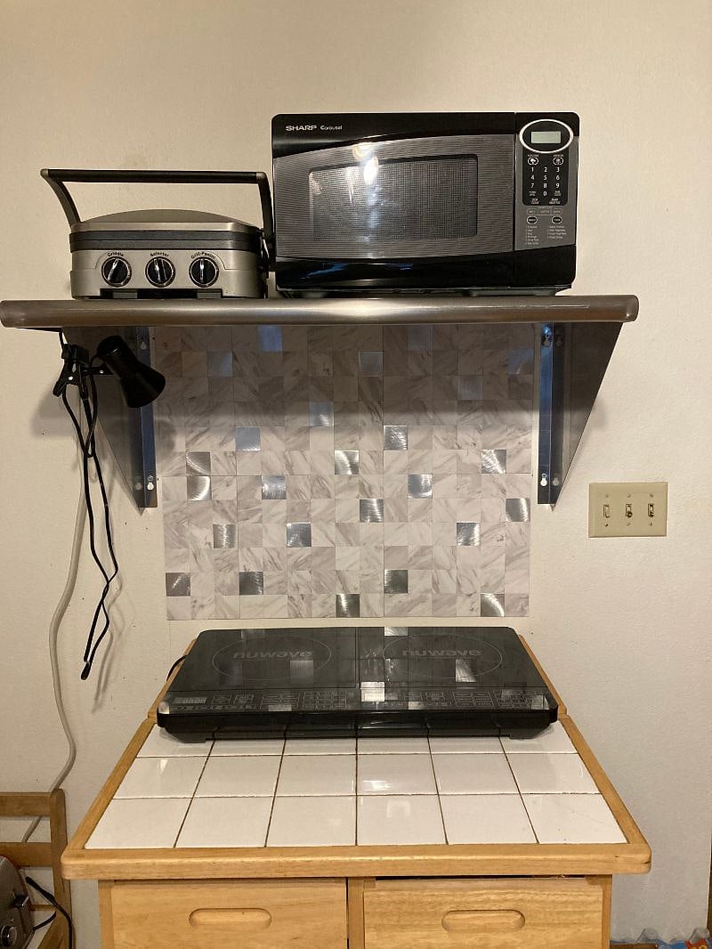 An induction double burner, with an electric grille and a microwave on the top shelf.