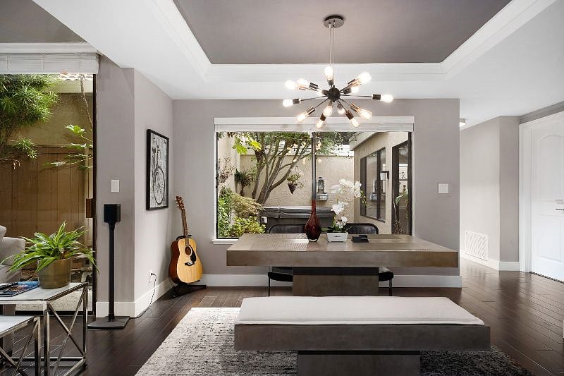 Step into a modern dining space anchored by a sleek concrete table and illuminated by a stylish chandelier.
A convenient mini bar enhances entertaining, while the large windows frame lush patio greenery, bringing a vibrant touch of nature indoors.