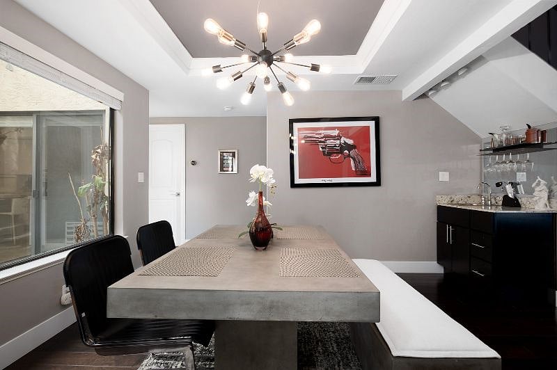 Step into a modern dining space anchored by a sleek concrete table and illuminated by a stylish chandelier.
A convenient mini bar enhances entertaining, while the large windows frame lush patio greenery, bringing a vibrant touch of nature indoors.
