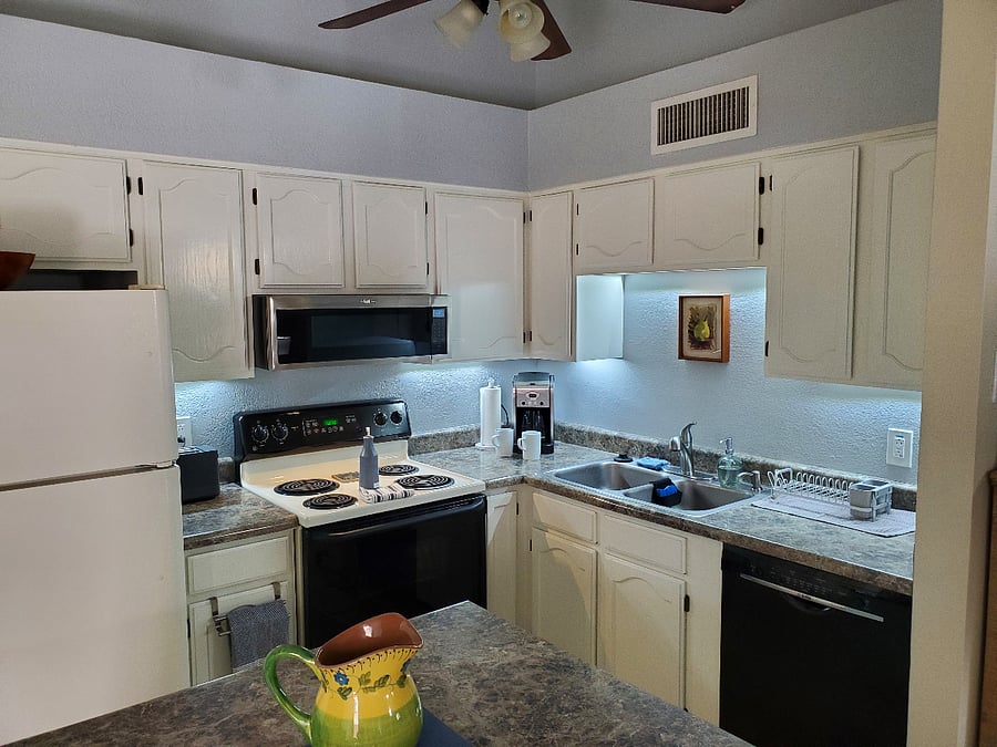 Bright, fully equipped kitchen with dishes, baking pans, appliances, and a sunlit island.