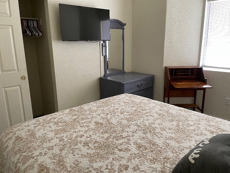 Front Bedroom. Queen bed, small desk, nightstand, dresser, mirror, overhead light with fan, lamp, blackout curtain, and smart TV.