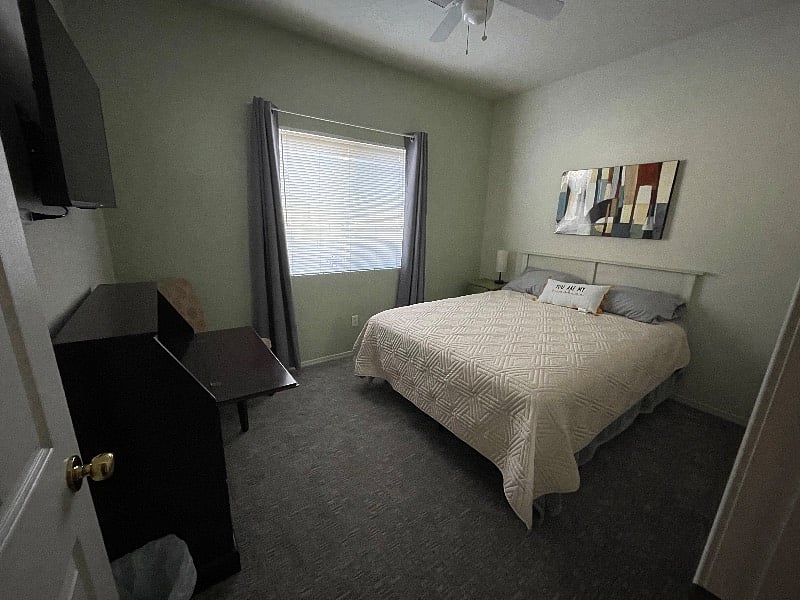 Back Bedroom. Queen bed, small desk, nightstand, dresser, mirror, overhead light with fan, lamp, and smart TV.