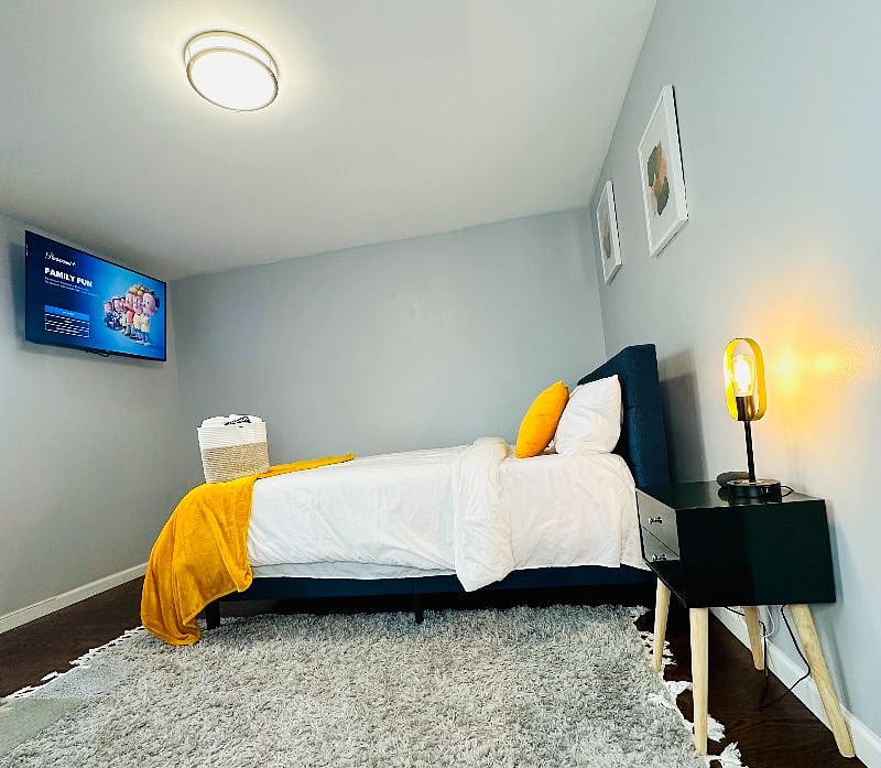 Bedroom 1 with a Queen-sized bed, 50-inch smart TV, charging lamp, virtual assistant/speaker, and en-suite bathroom