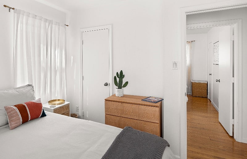 Wood dresser, closet, hangers for clothing storage. White linen-blend curtains on brass colored curtain rods. Mid-century modern color palette accented by natural jute, brass and grays.