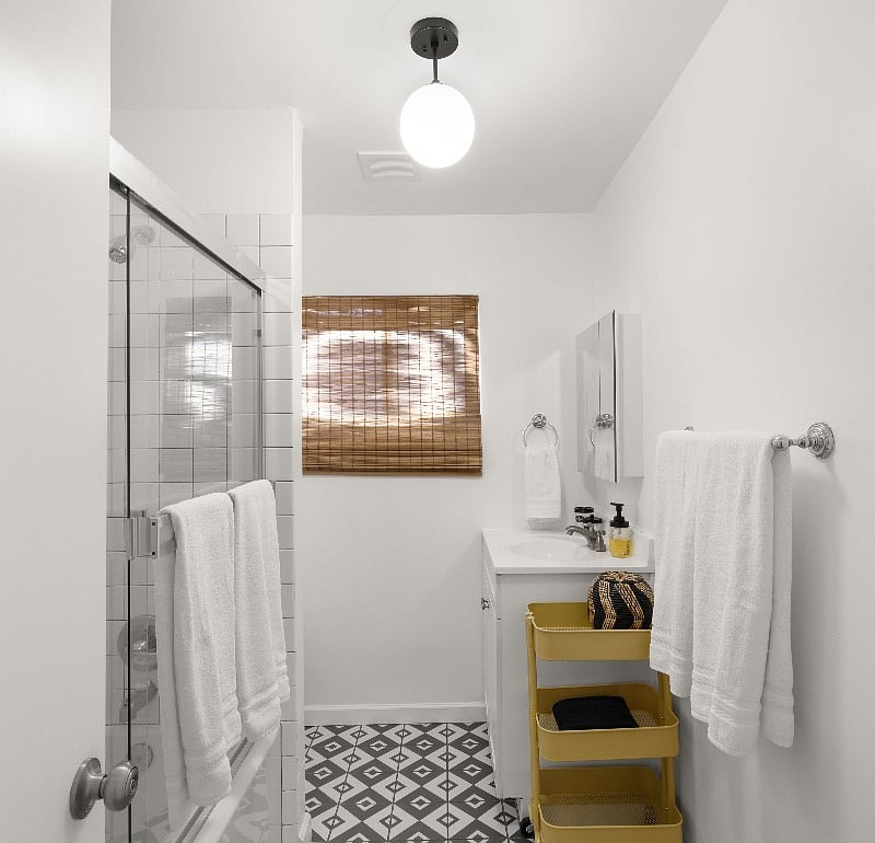 Full bathtub and shower combo with glass doors. Mirrored medicine cabinet and bathroom cart provides ample storage for toiletries.