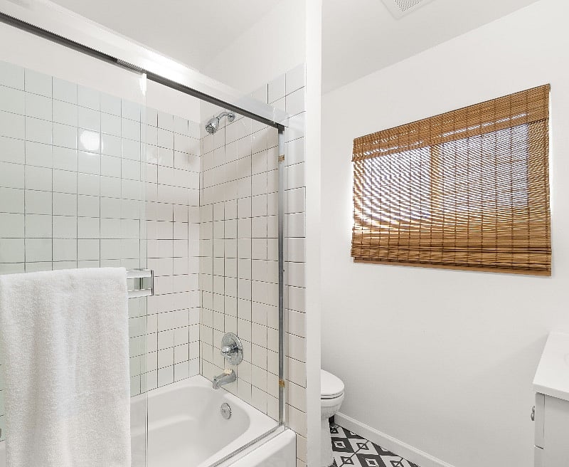 Natural bamboo cordless shades. White tiled shower/tub area.