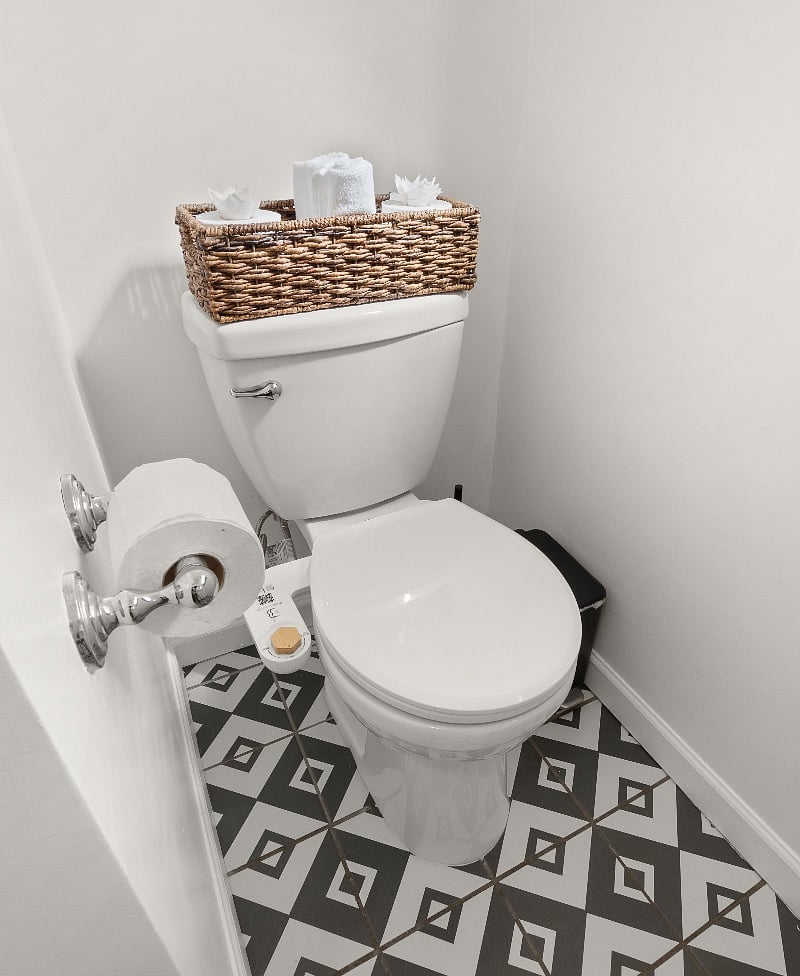 Wicker basket for storage of wash cloths and extra TP. Better Butts toilet bidet and TP made from recycled material to save trees. No-touch black metal trash can.