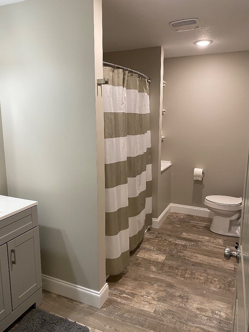 Large full bath with tub shower, well lit vanity and shelves for storage.