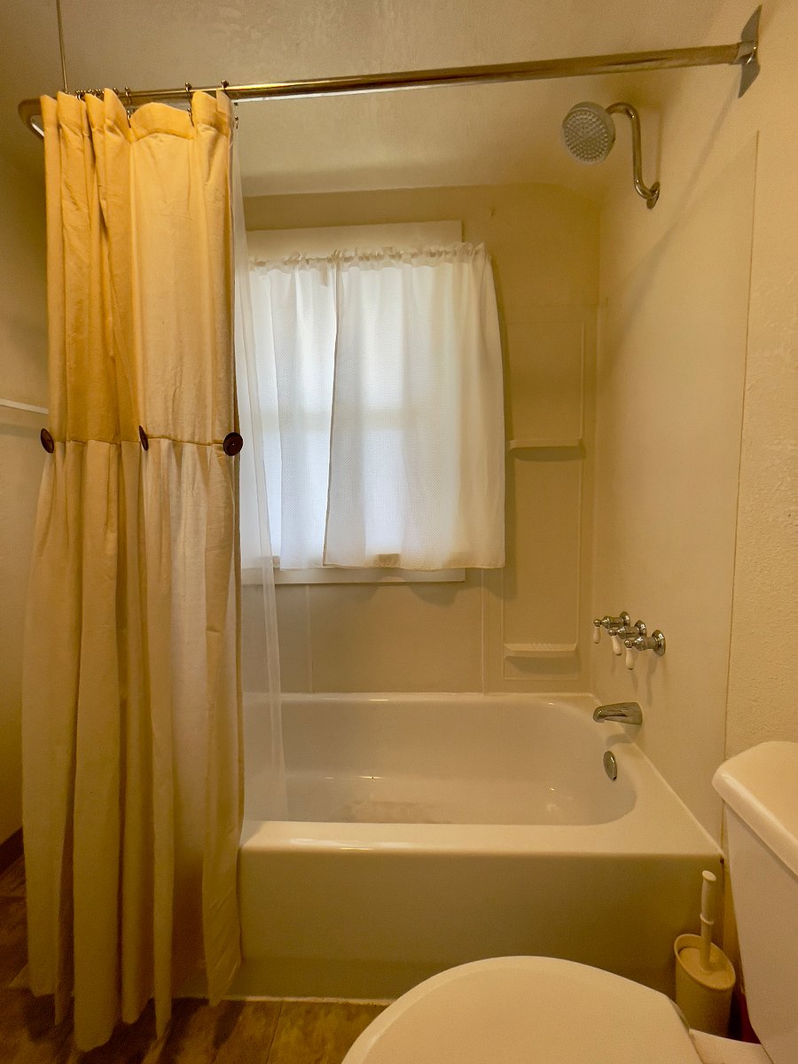 Tub and shower with wrap-around curtain and opaque window for natural lighting and privacy.