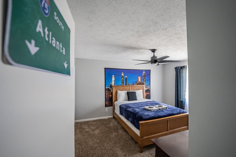 Cozy bedroom with comfortable bedding, ceiling fan, and fun Atlanta-themed decor.