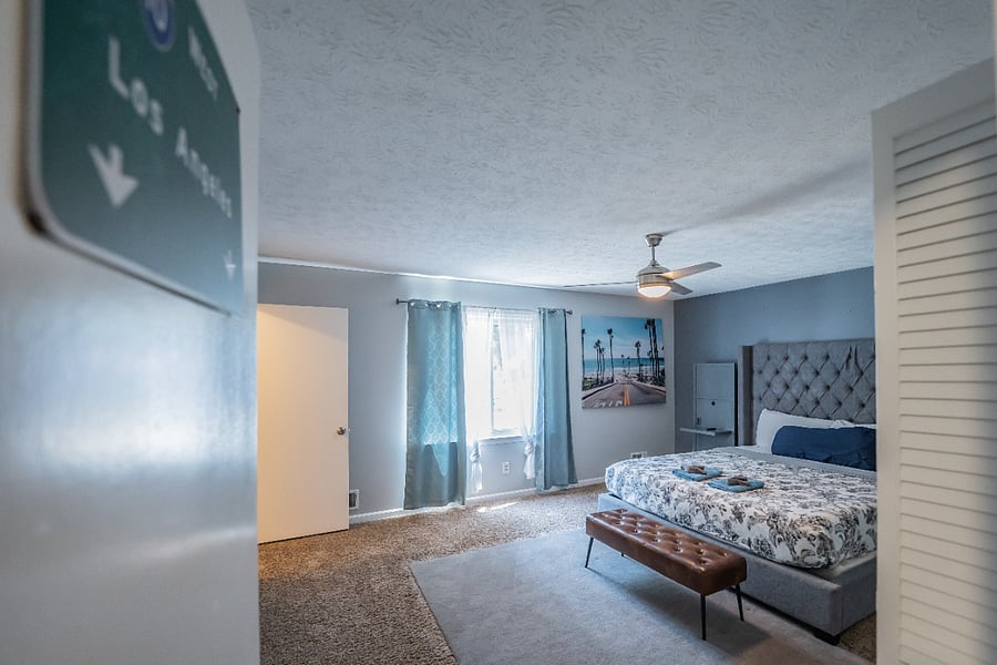 Inviting bedroom with an upholstered headboard, a bench at the foot of the bed, and bright natural light.
