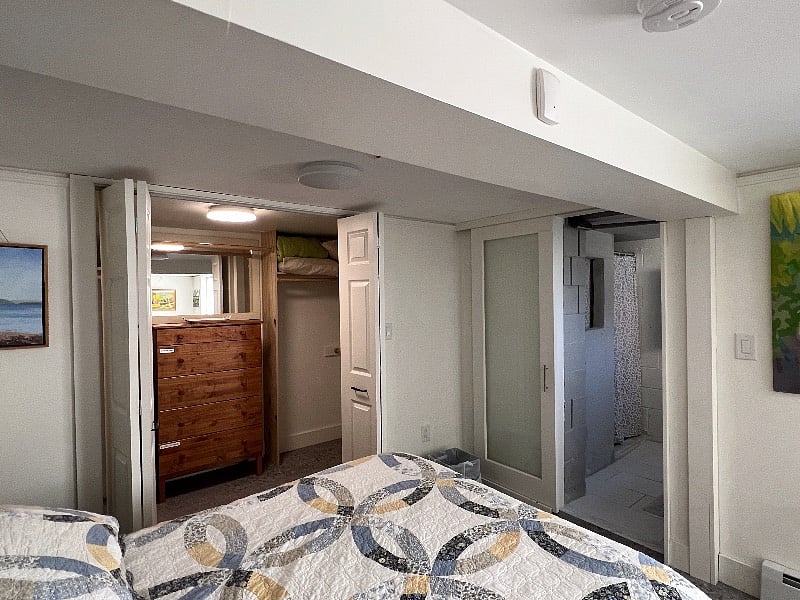 Walk-in closet doors open, mirror above wood dresser.