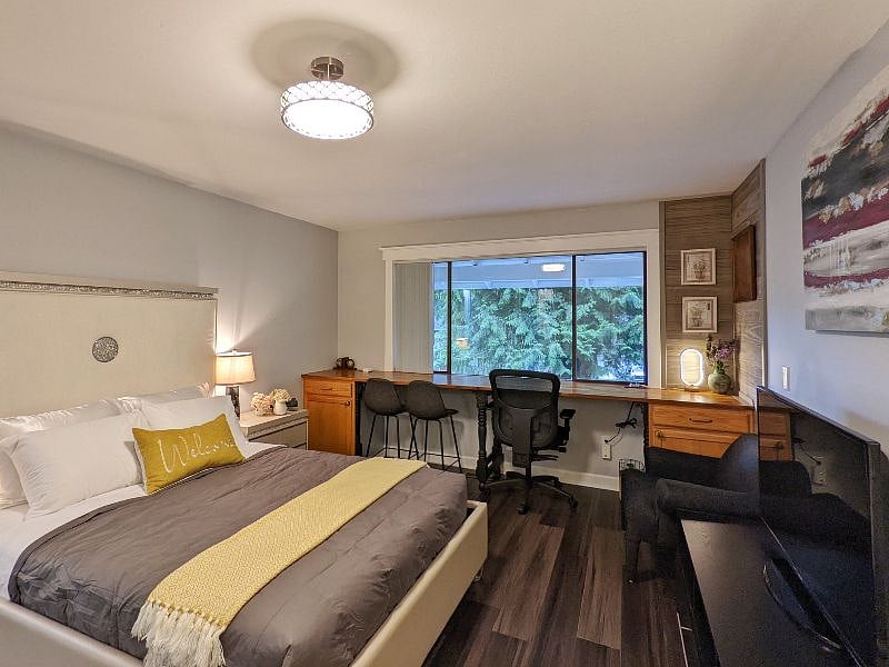 A luxury queen bed set with a long desk for at-home work, with a flat-screen TV.