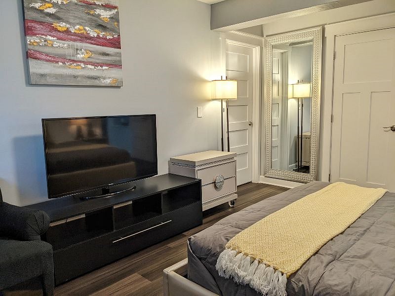 A flat-screen TV with artwork, a closet and a fancy mirror.
