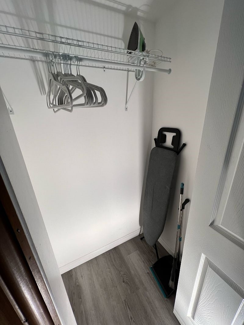 Living room closet stocked with hangers, iron, ironing board and broom. 