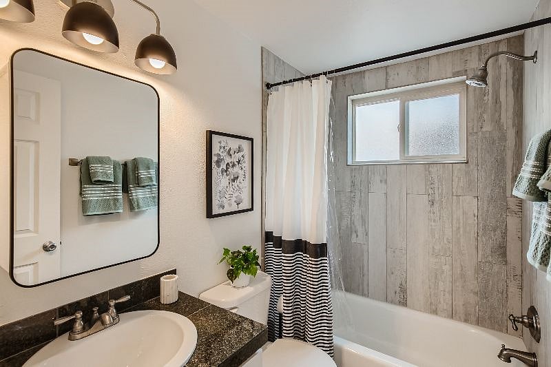 The updated bathroom features an all new vanity, light fixture, modern mirror, and trendy tile surround in the tub/shower combo.
