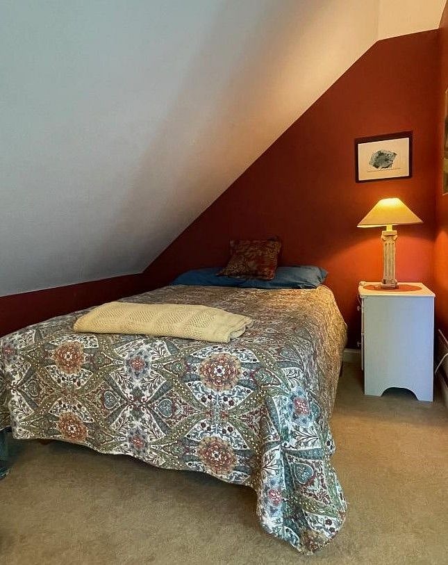 Back bedroom, faces east: full mattress on wood platform, nightstand, sloping ceiling