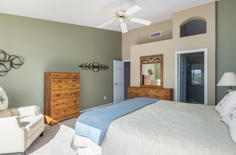 Primary bedroom with king sized bed, bedside tables with lamps, and two dressers.  Seating by backyard window.  Walk in closet off of bathroom.