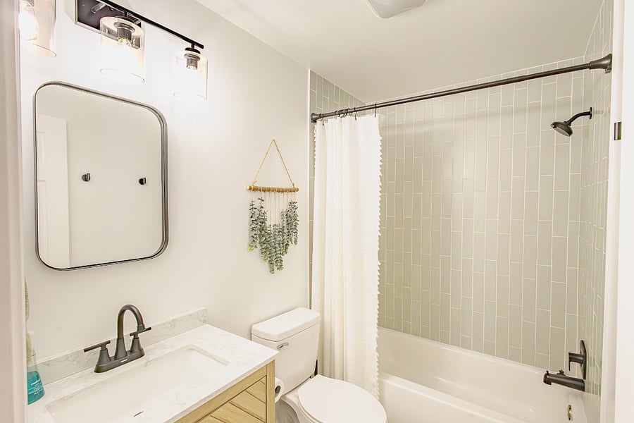 Renovated bathroom with tub-shower combo, sage tile surround, marble-top vanity, and modern fixtures.