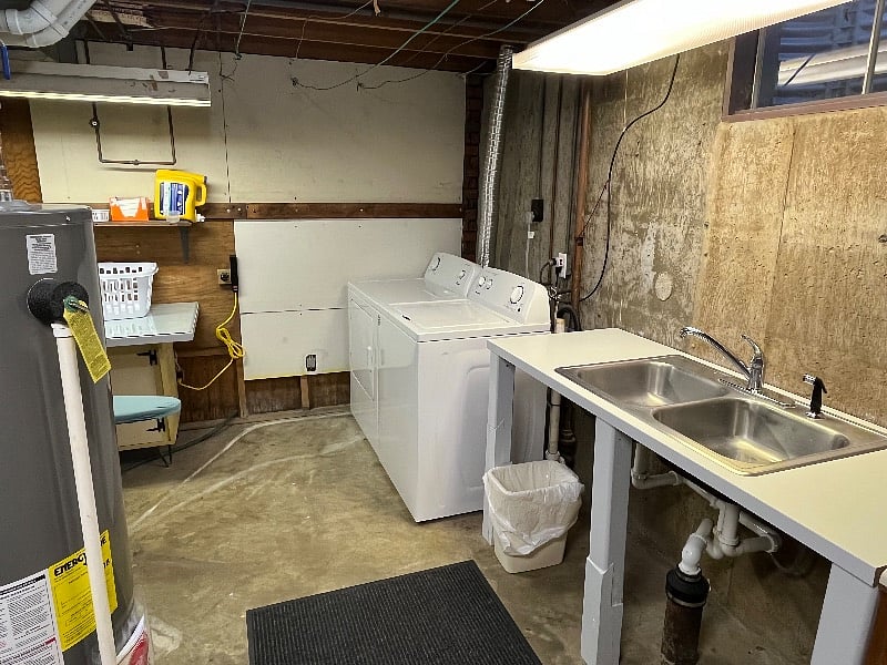 Utility room is located in the basement and includes washer, dryer, sink, iron, and ironing board. 