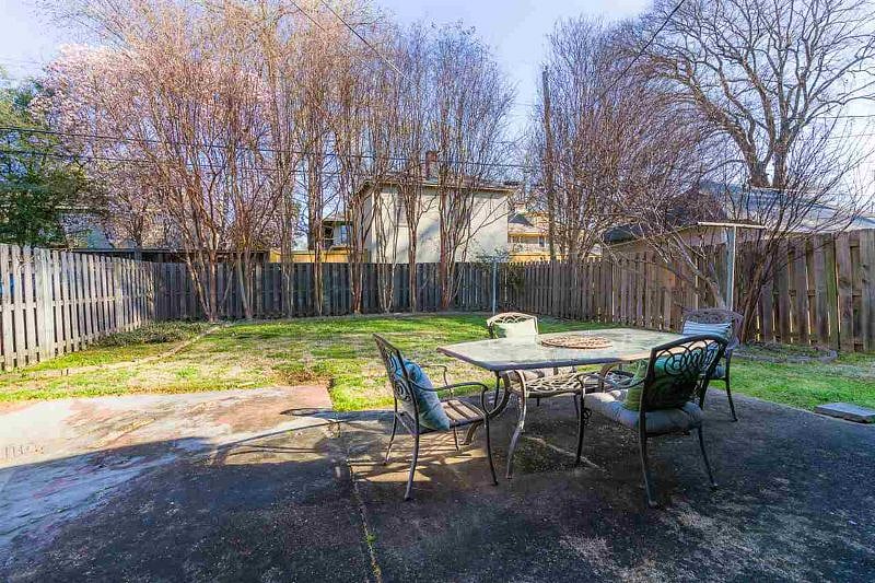 Fully fenced backyard with a patio, outdoor dining table, and seating areas lined by crepe myrtles.